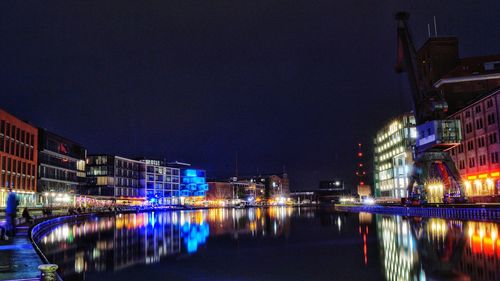 Illuminated buildings by river against sky at night