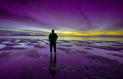 Silhouette man standing at beach against purple sky during sunset