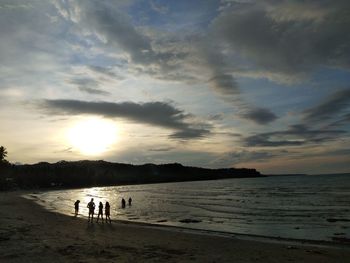 People on beach against sky during sunset