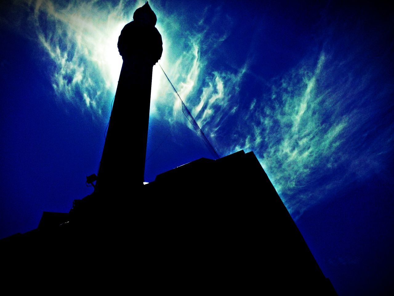 low angle view, silhouette, built structure, architecture, sky, building exterior, cloud - sky, tower, dusk, tall - high, outline, blue, cloud, street light, outdoors, city, no people, building, tall, sunset