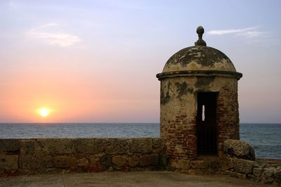 Dome of old building by sea against sky during sunset