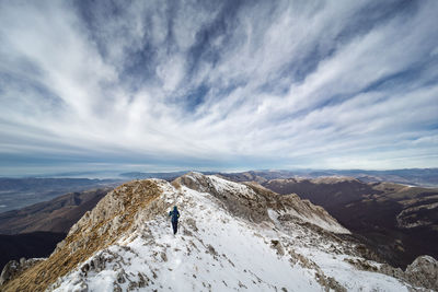 Rear view of woman on snowcapped mountain against cloudy sky