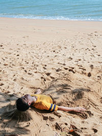 High level view of a boy burying himself with sand on the beach