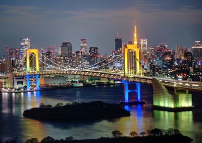 Illuminated rainbow bridge with cityscape in background at night