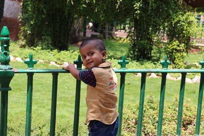 Portrait of smiling boy standing by railing at park