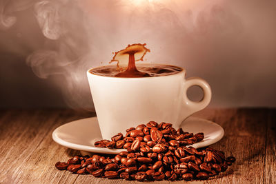 Close-up of splashing coffee in cup with beans on table