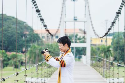 Side view of man photographing while standing on bridge