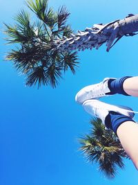 Low section of woman standing by palm tree against blue sky