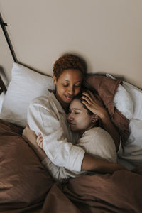 Non-binary couple embracing each other while lying on bed at home