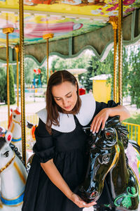 Beautiful brunette girl in a black dress poses on a bright carousel with horses