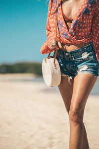 Girl walks along the beach with a rattan bag on her shoulder