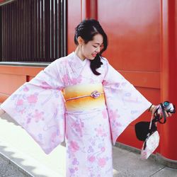 Young woman looking away while standing against wall