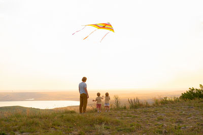 Happy man and children, father and sons, with kite in nature at sunset