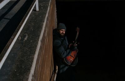 High angle portrait of young man playing guitar against wall