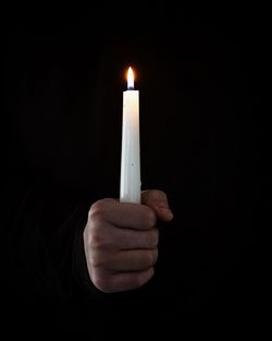 Close-up of hand holding illuminated candle against black background