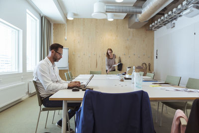 Mature businessman using laptop at conference table with coworker in background