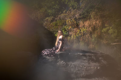 Woman standing on rock against waterfall in forest