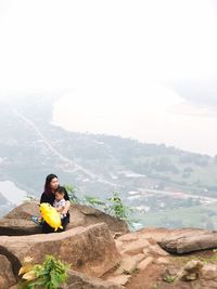 Woman with child sitting on rock against sky at mountain