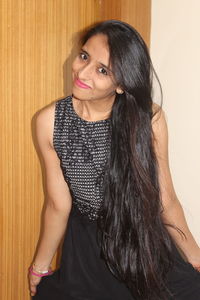 Portrait of smiling beautiful woman in black dress standing against wall at home