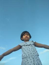 Low angle portrait of girl standing against clear blue sky