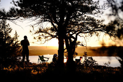 Silhouette man standing at lakeshore during sunset