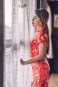 Young woman looking away while standing against window