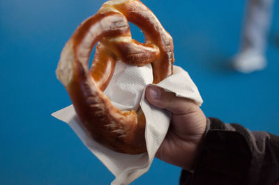 Cropped hand of person holding food against blue background