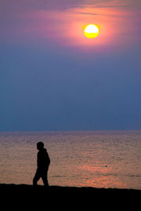 Silhouette man standing on beach against sky during sunset