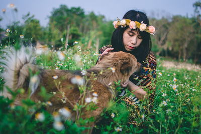 Woman wearing flowers while sitting with dog on field 