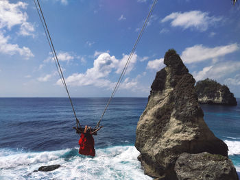Rear view of woman sitting on swing over sea against sky