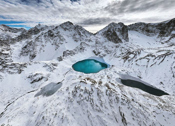 Three mountain frozen turquoise lakes in the snowy mountains, top view from a drone