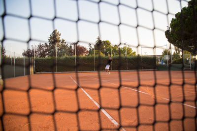 Man playing tennis on court seen through net