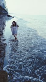 Rear view of woman walking in sea against clear sky