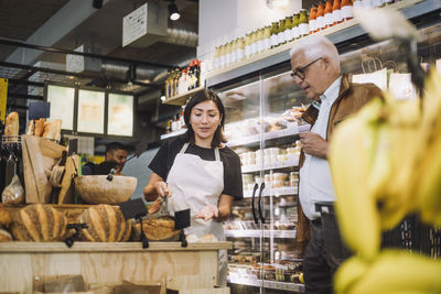 Saleswoman discussing over bread with senior male customer in grocery store