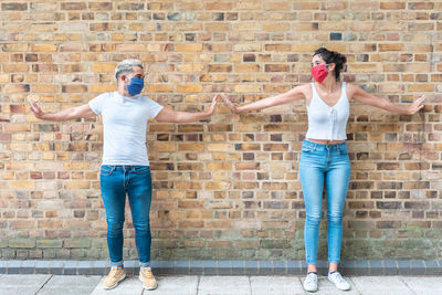 Full length of couple wearing mask standing against wall