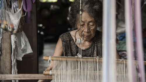 Senior woman weaving loom in factory