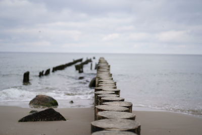 Wooden posts in sea against sky