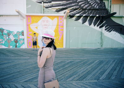 Portrait of mid adult woman wearing sunglasses standing on road against building 