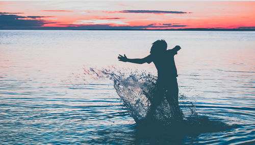 Silhouette person jumping in sea against sky during sunset