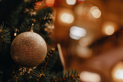 Golden christmas ball hanging on the christmas tree. defocused garland lights, bokeh magic effect.