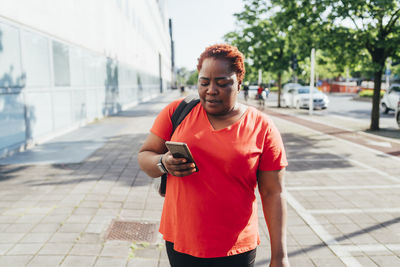 Woman using smart phone walking on footpath