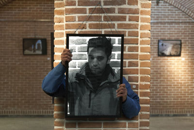 Portrait of young man sitting against brick wall