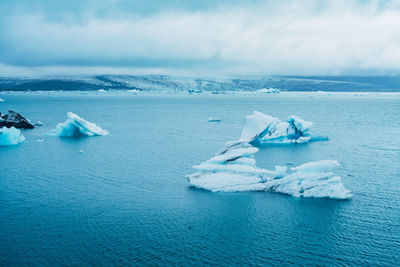 Glacier in lake against cloudy sky