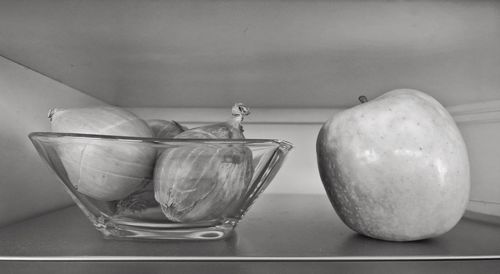 Close-up of onions in bowl and apple on shelf