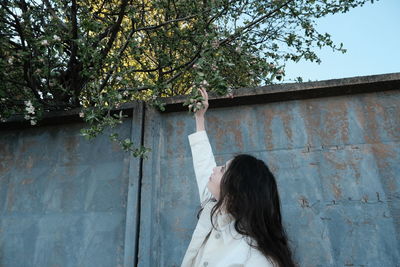 Woman standing by tree against wall