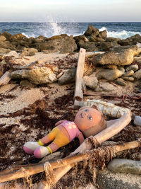 Portrait of doll lying on rock by sea shore