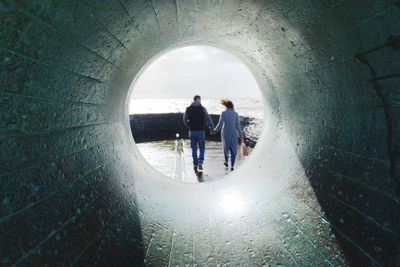 Rear view of couple holding hands walking against sea