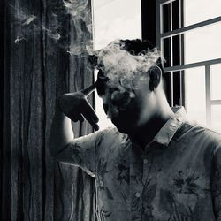 Portrait of young man smoking by window