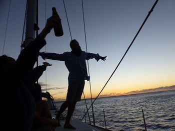Silhouette man sailing in sea against sky during sunset