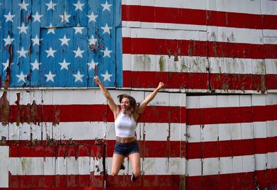 Excited woman jumping against american flag painted on wall